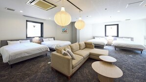 A hotel room with two single beds, a sofa, a round coffee table, and a large window providing a view.