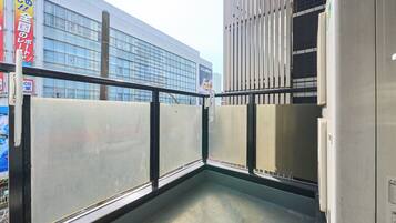 A balcony with a metal railing, a concrete floor, and a view of a modern building with large windows.