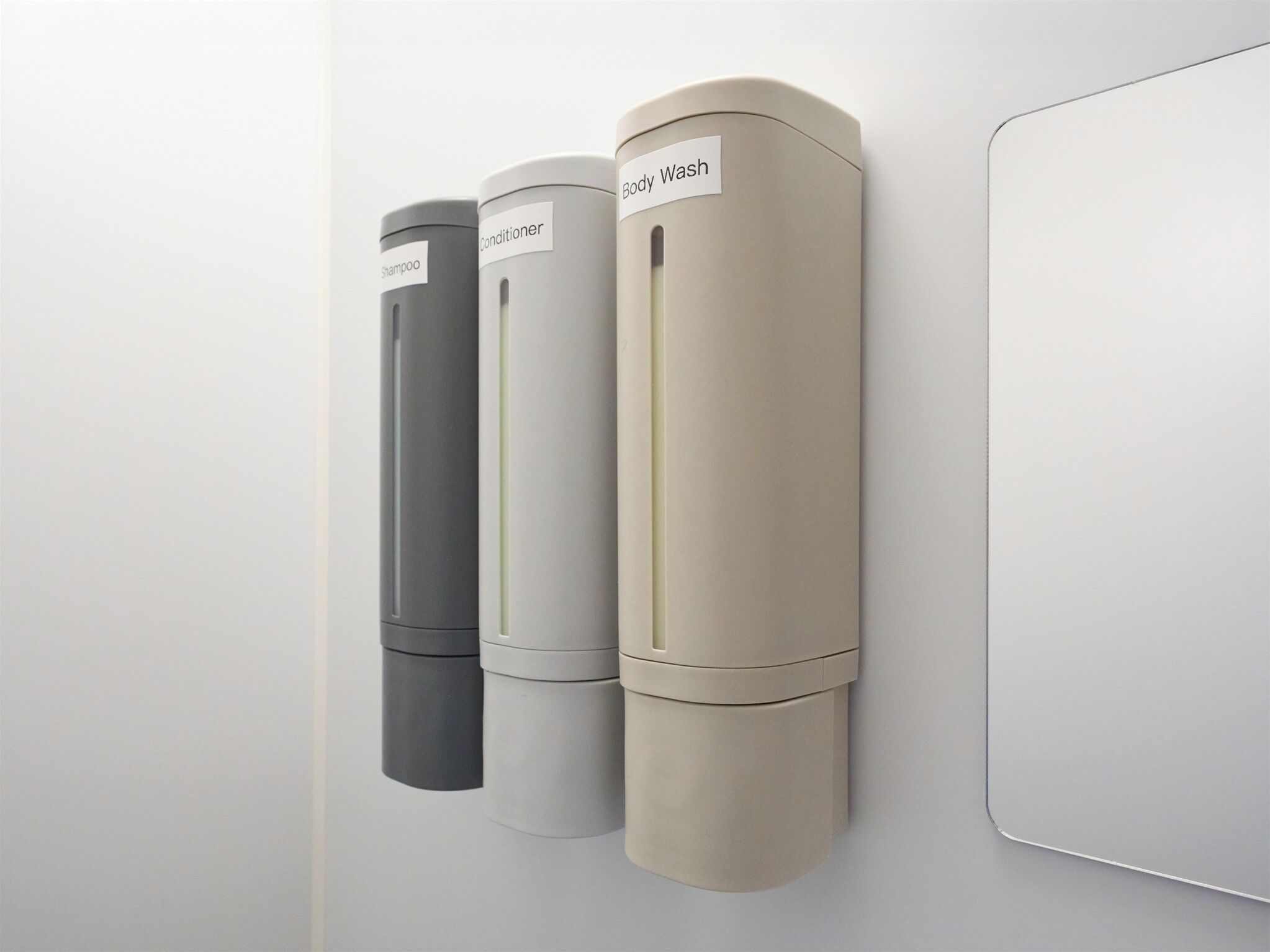 Three cylindrical dispensers labeled for shampoo, conditioner, and body wash mounted on a wall.