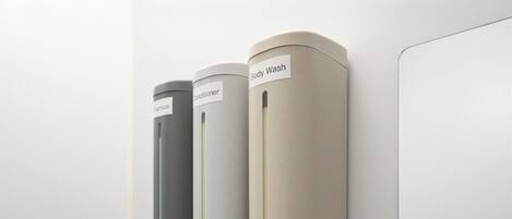 Three cylindrical dispensers labeled for shampoo, conditioner, and body wash mounted on a wall.