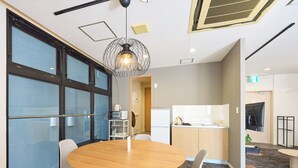 A modern meeting room with a round wooden table, two grey chairs, a unique wireframe pendant light, and large windows with blinds.