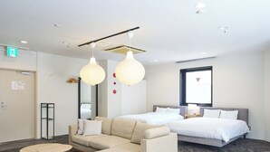 A hotel room with a sofa, two beds, a round coffee table, and pendant lights.