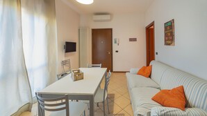 A dining area with a table and chairs, a sofa with orange pillows, a television, and a door.