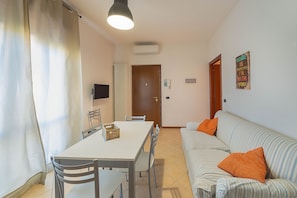 A dining area with a table and chairs, a sofa with orange pillows, a television, and a door. - Casa Laura, Torri del Benaco (Torri Del Benaco)