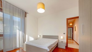 A bedroom with a bed, bedside tables, a hanging lamp, and a door leading to another room.