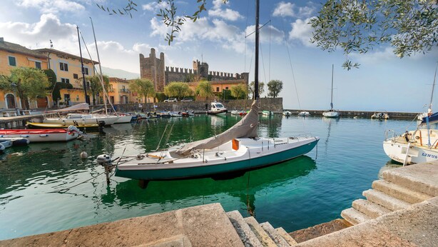 A marina with boats docked, a castle in the background, and stone steps leading down to the water.