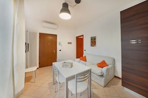 A small, well-lit room with a dining table, chairs, a sofa, and a wooden wardrobe. - Casa Laura, Torri del Benaco (Torri Del Benaco)