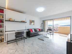 A modern living room with a sofa, coffee table, and a dining area. There is a balcony with a view of the city. - Studio in a Prestigious Residence, Close to the City Centre (Cannes)