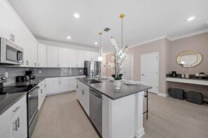 A modern kitchen with white cabinets, a central island, stainless steel appliances, and pendant lighting. - Lakeview LUX Pool VR Villa Champions Gate Retreat (Davenport)
