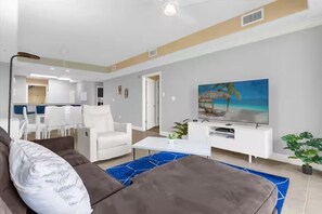 Ein modernes Wohnzimmer mit Sofa, Couchtisch und Fernseher. Im Hintergrund befindet sich ein Essbereich mit Stühlen und einem Tisch.