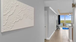 Un pasillo con pared texturizada, una puerta que da a un balcón con piscina y vistas al exterior.