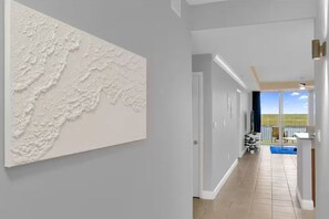 Ein Flur mit strukturierter Wand, einer Tür zu einem Balkon mit Pool und Blick ins Freie.