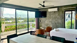 Una camera d'albergo moderna con balcone, un letto, una TV e un'area pranzo.