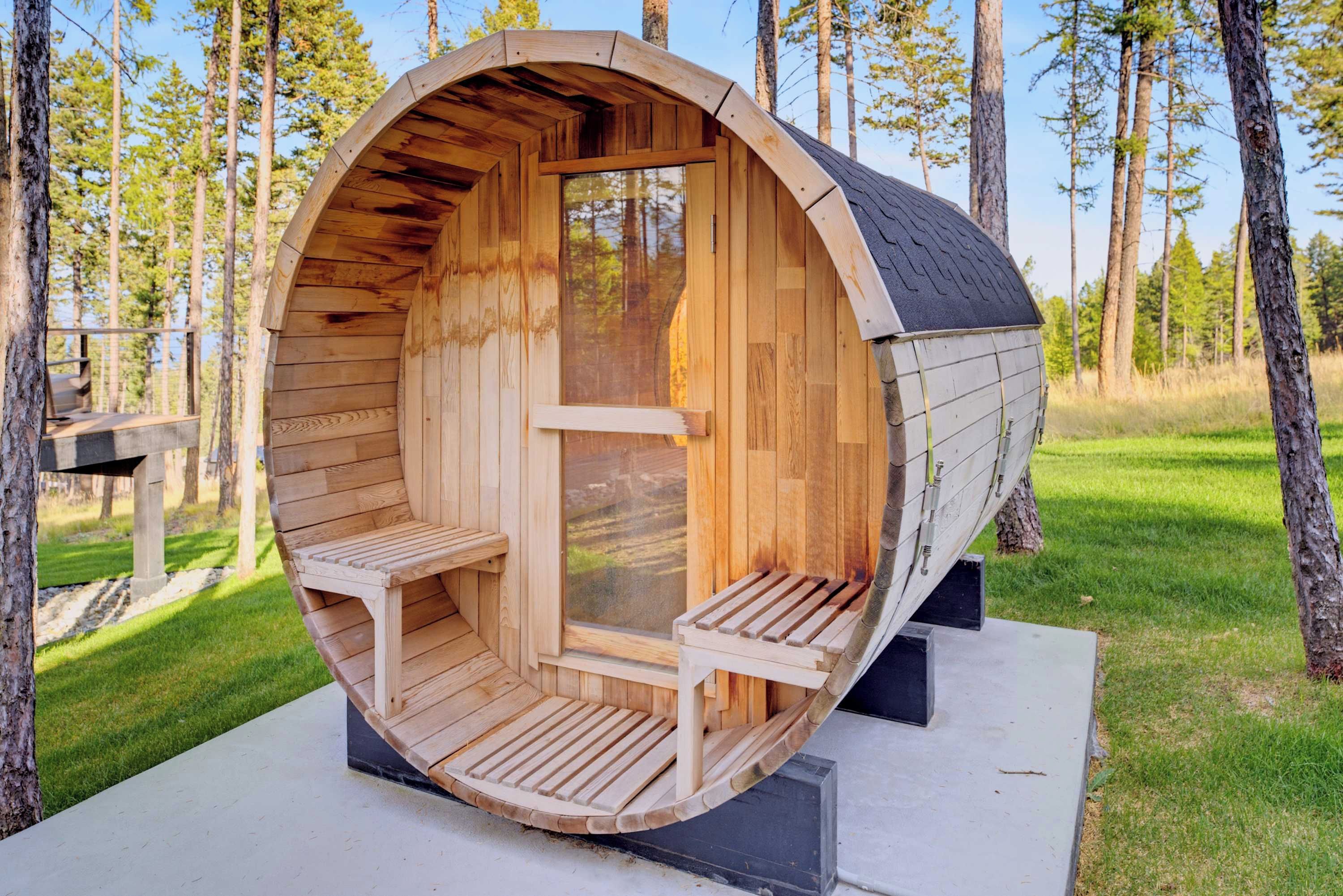 A wooden cylindrical structure with a bench and a table inside, surrounded by trees.
