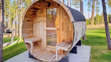 A wooden cylindrical structure with a bench and a table inside, surrounded by trees.
