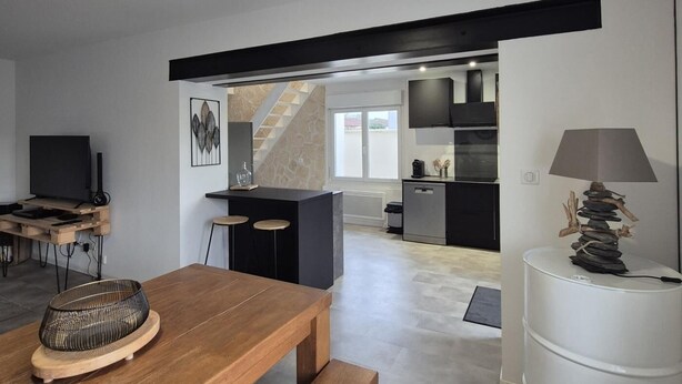 A modern kitchen with a black countertop, a dining area with a wooden table, and a kitchen island with stools. - Charming house between the countryside and the sea (SAINT NAZAIRE SUR CHARENTE)