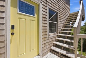 Eine gelbe Tür mit einem Fenster darüber, eine Treppe aus Holz und ein Holzzaun.