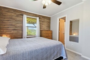 Une chambre à coucher avec un lit, une commode en bois, une porte et un ventilateur de plafond.
