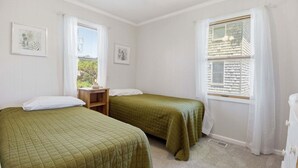 Een kamer met twee bedden, een plafondventilator en een raam met jaloezieën.