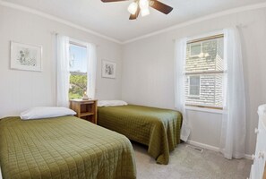 Ein Zimmer mit zwei Betten, einem Deckenventilator und einem Fenster mit Jalousien.