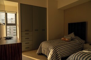 A bedroom with a bed, a dresser, a wardrobe, and a window with a view of buildings. - Sunlit & Sea View (Mazatlán)