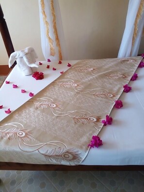 A bed with a decorative headboard, a white towel, and pink flower petals. - Hotel Rafiki Malindi (Malindi)