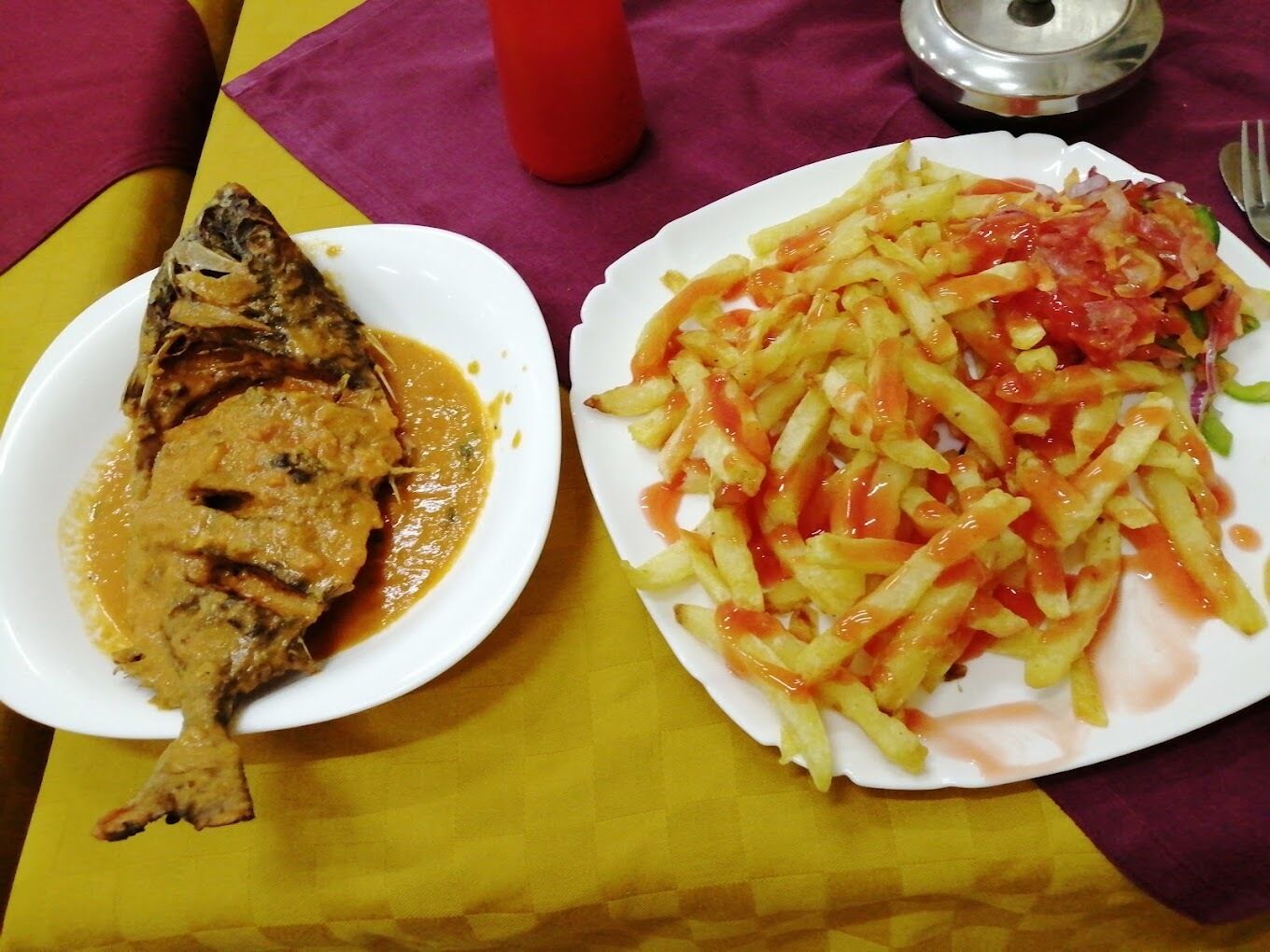 Un repas composé d’un poisson grillé avec une sauce, accompagné d’une assiette de frites, de ketchup et de légumes.