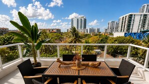 A balcony with a wooden table and chairs, surrounded by potted plants and a city view. - Hollywood Luxury Gem - 3 king beds - pool - gym - near ocean (Hollywood)