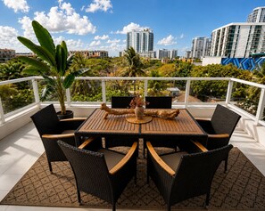 Ein Balkon mit Holztisch und -stühlen, umgeben von Blumentöpfen und Blick auf die Stadt.