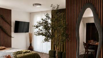 Een moderne slaapkamer met een bed, een grote spiegel, een potplant en een televisie.