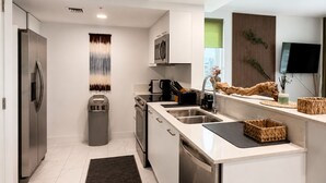 A modern kitchen with stainless steel appliances, a built-in oven, a dishwasher, and a large window providing natural light. - Hollywood Luxury Gem - 3 king beds - pool - gym - near ocean (Hollywood)