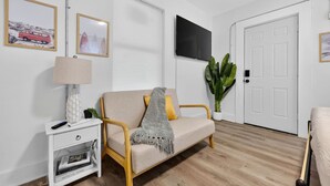 Een woonkamer met een bank, een televisie, een lamp en een plant.