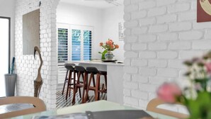 Une cuisine moderne avec des murs en briques blanches, un coin repas avec des chaises en bois et une fenêtre équipée de stores.
