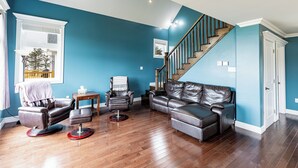 Een woonkamer met een blauwe muur, een leren bank, een leren fauteuil, een kleine tafel en een trap.