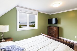 Un dormitorio con cama, cómoda, televisor y ventana con vista al mar.