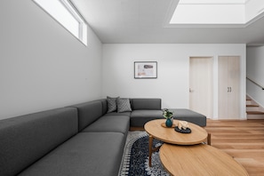 Un salon moderne avec un canapé d’angle gris, une table basse ronde en bois et un tapis bleu.