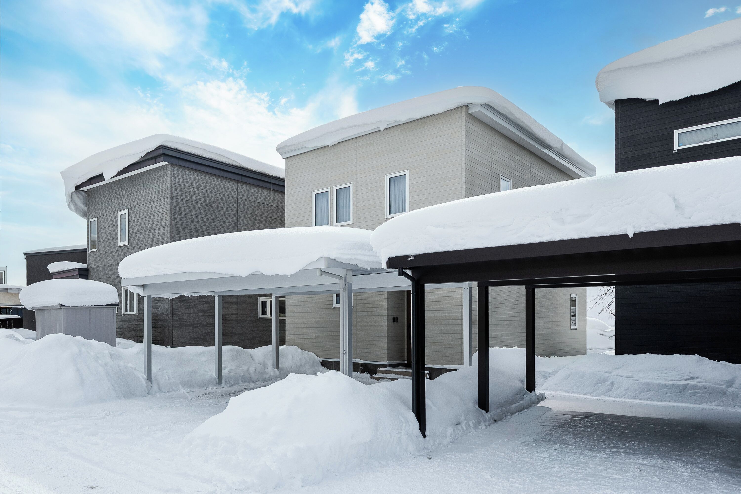 Zona residencial con varias casas cubiertas de nieve, que presentan arquitectura moderna y un cielo despejado.
