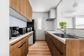 Une cuisine moderne avec des meubles en bois, un plan de travail blanc, un évier en acier inoxydable et une machine à café.