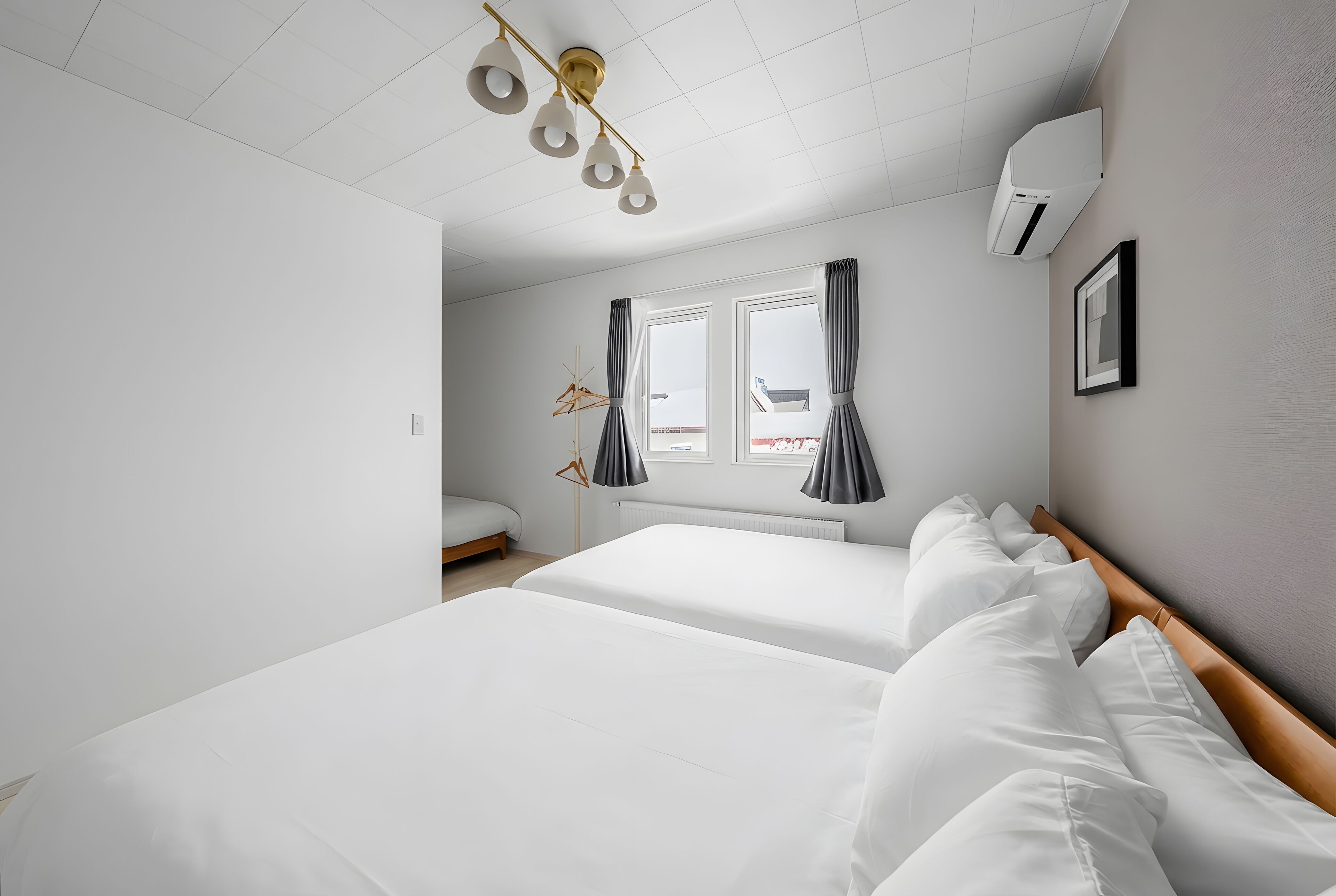 A hotel room with two beds, a window with curtains, a radiator, and a ceiling light fixture.