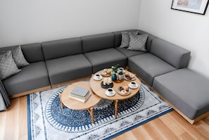 Un salon moderne avec un canapé d’angle gris, une table basse ronde en bois et un tapis à motifs.