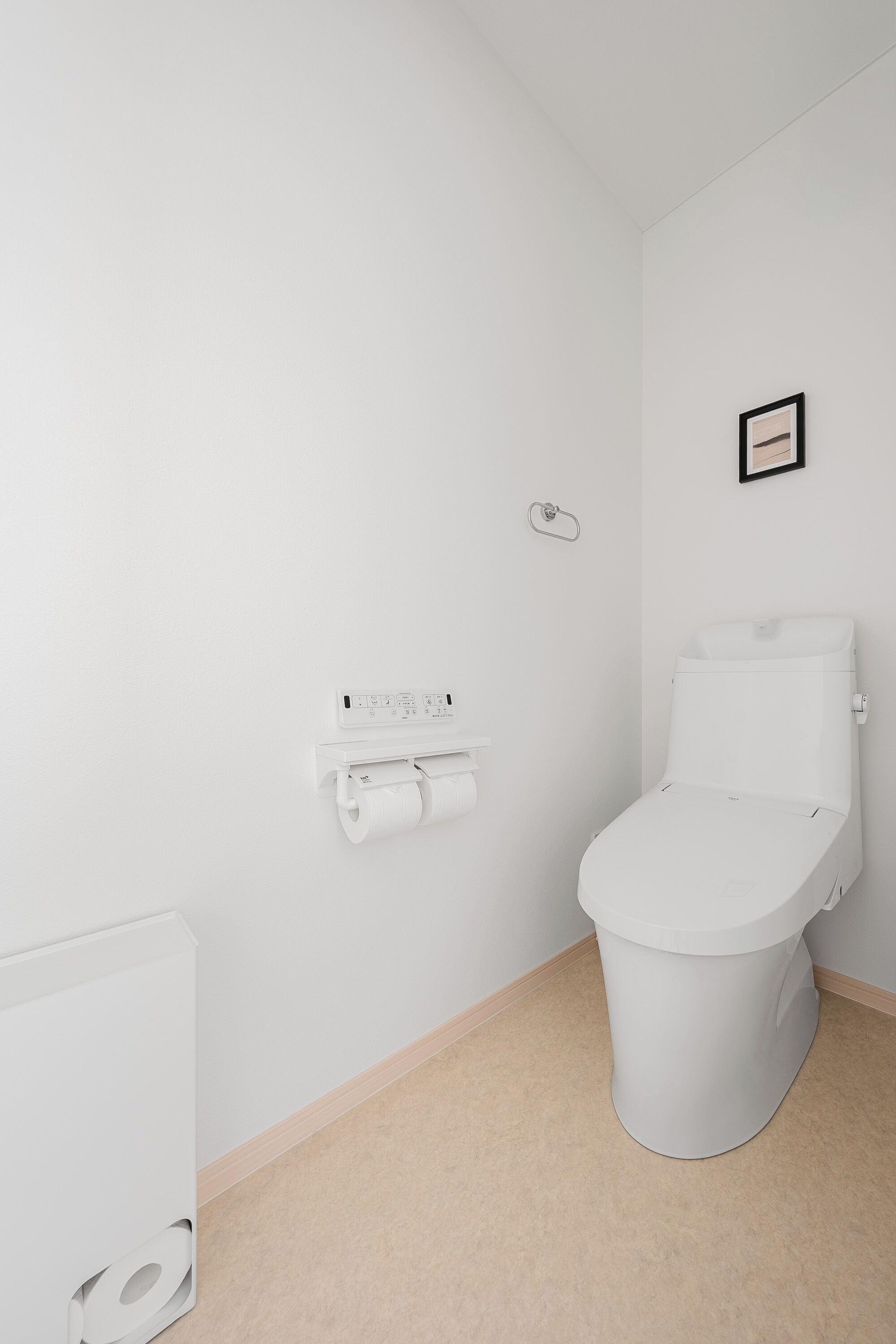 A modern bathroom with a toilet, a toilet paper holder, and a framed picture on the wall.