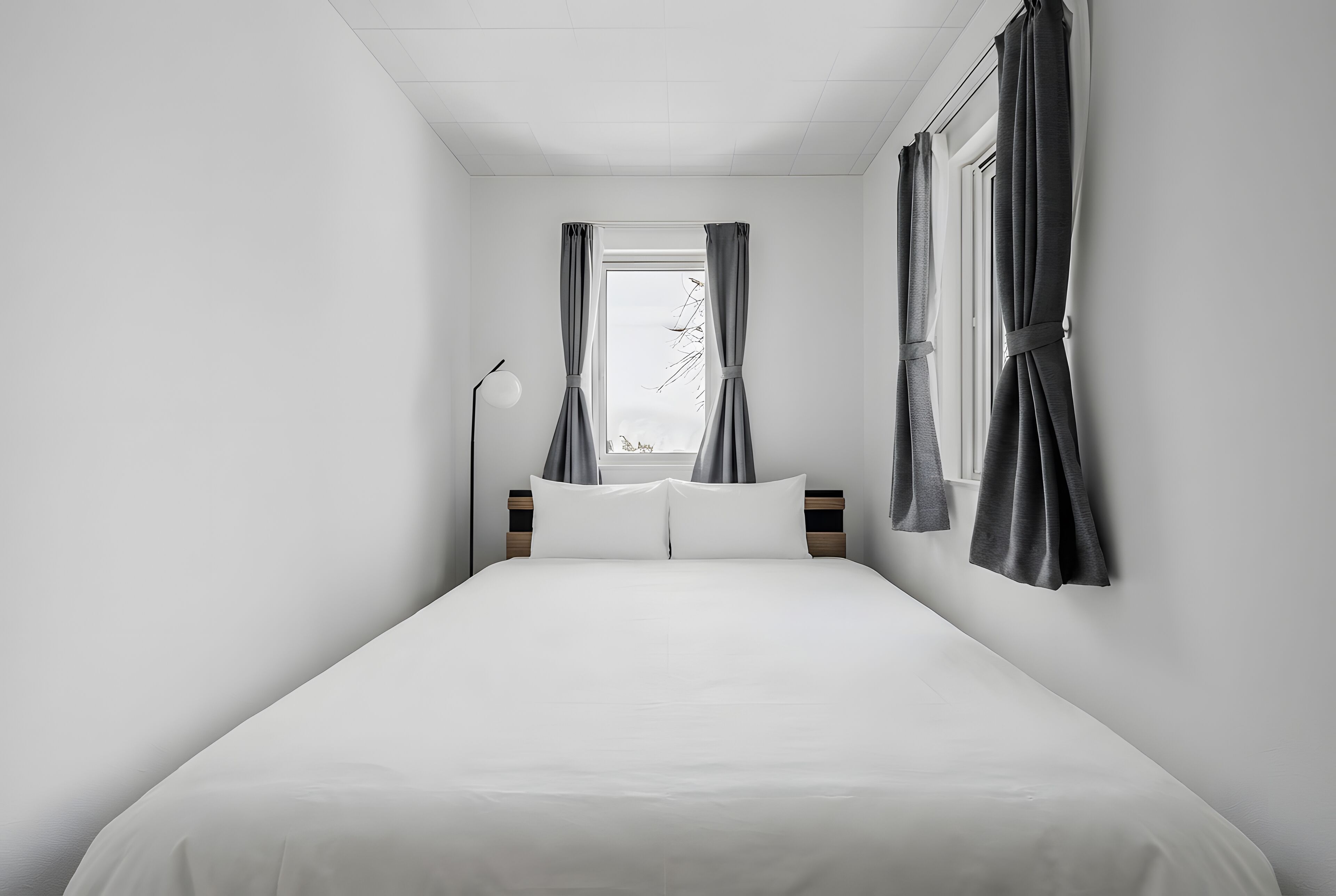 Minimalistiseen tyyliin sisustettu hotellihuone, jossa on suuri sänky, yöpöytä ja ikkuna, jossa on verhot.