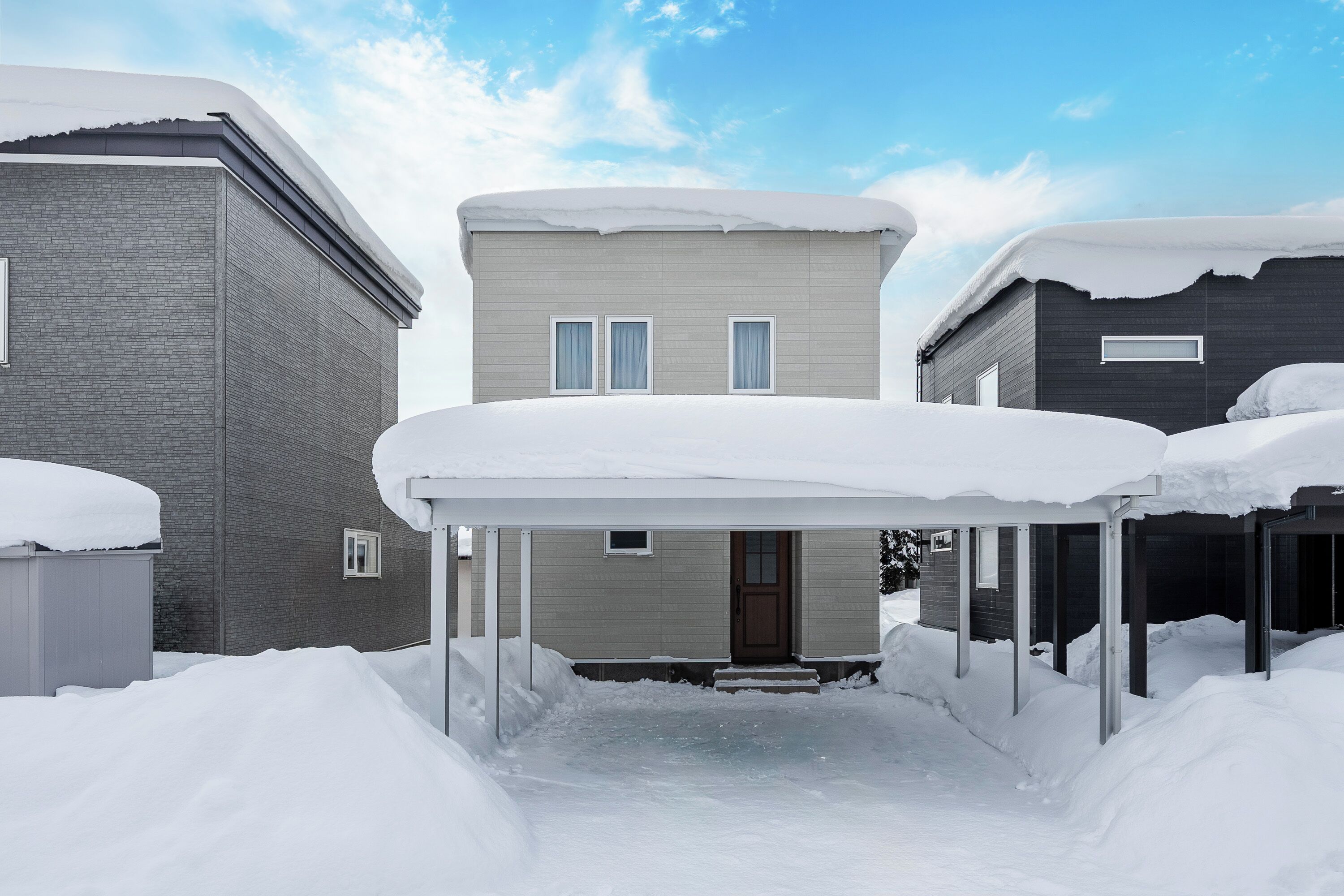 Un quartiere residenziale con tre case coperte di neve, un porticato e un cielo sereno.
