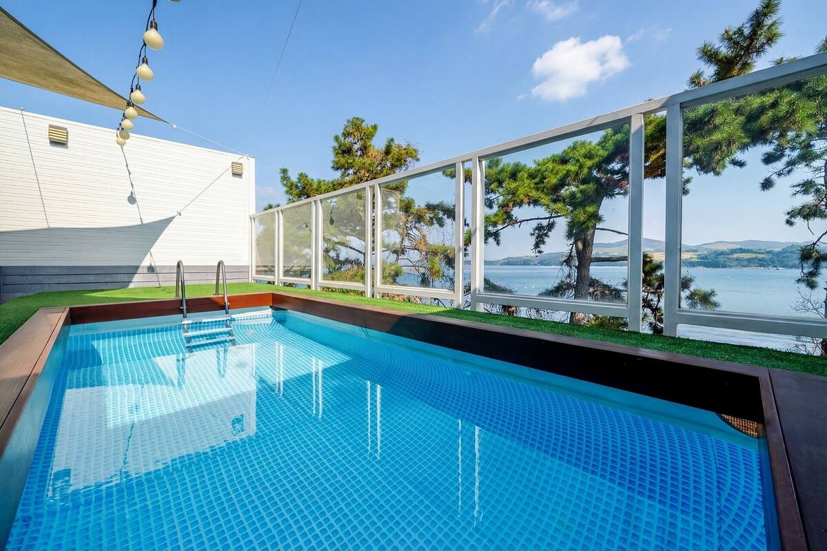 Una piscina con vistas a un lago, rodeada por un edificio blanco y árboles.