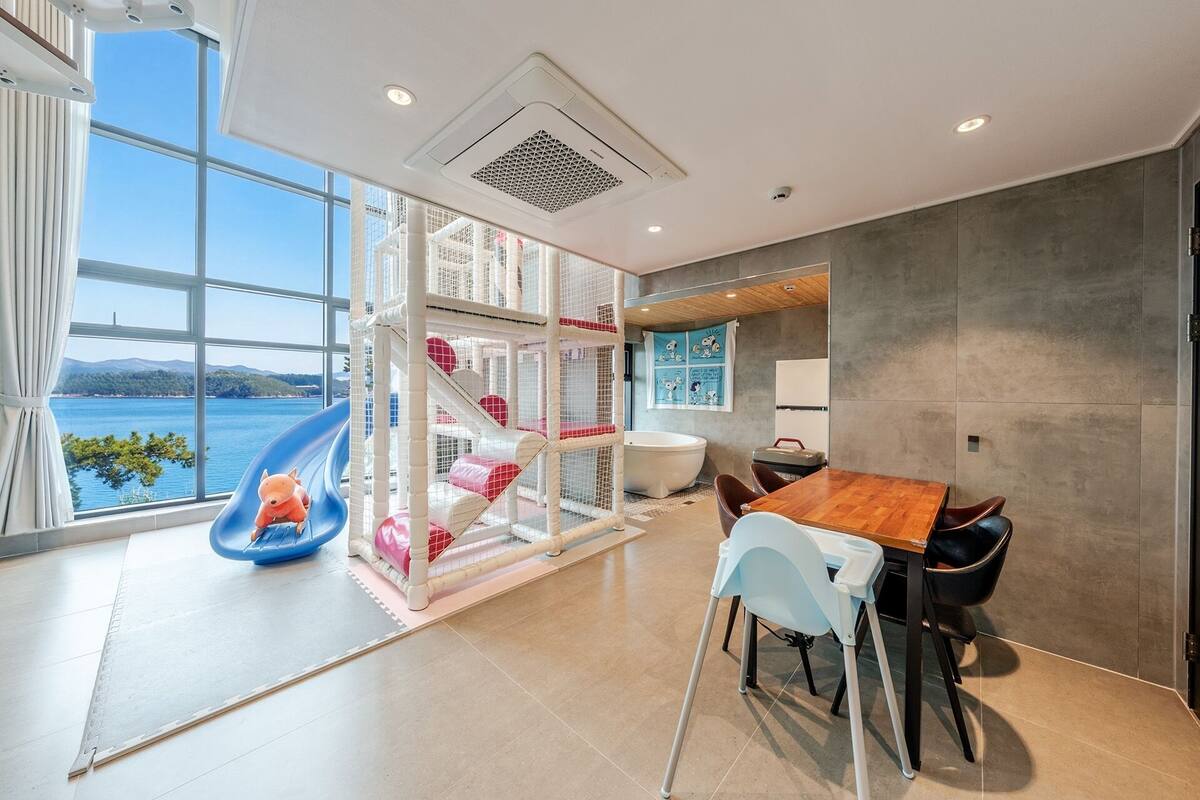 Un interior moderno con vistas al mar, un área de juegos, un comedor y una bañera grande.