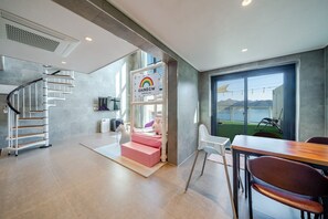 A modern interior with a staircase, a play area, a dining area, and a large window offering a view of the water. - Geoje Rainbow Kids Pool Villa (Geoje)