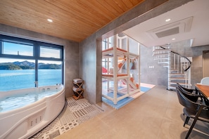 Un baño moderno con una bañera grande, techo de madera y vista al mar.