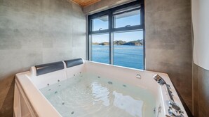 A modern bathroom with a large bathtub, a window with a view of the sea, and wooden ceiling. - Geoje Rainbow Kids Pool Villa (Geoje)