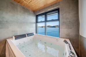 A modern bathroom with a large bathtub, a window with a view of the sea, and wooden ceiling. - Geoje Rainbow Kids Pool Villa (Geoje)