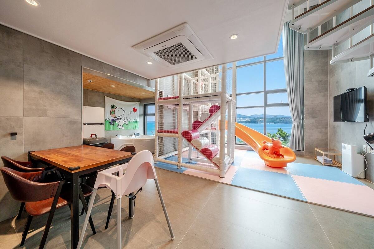 Un interior moderno con zona de comedor, estructura de juegos y un ventanal con vistas.